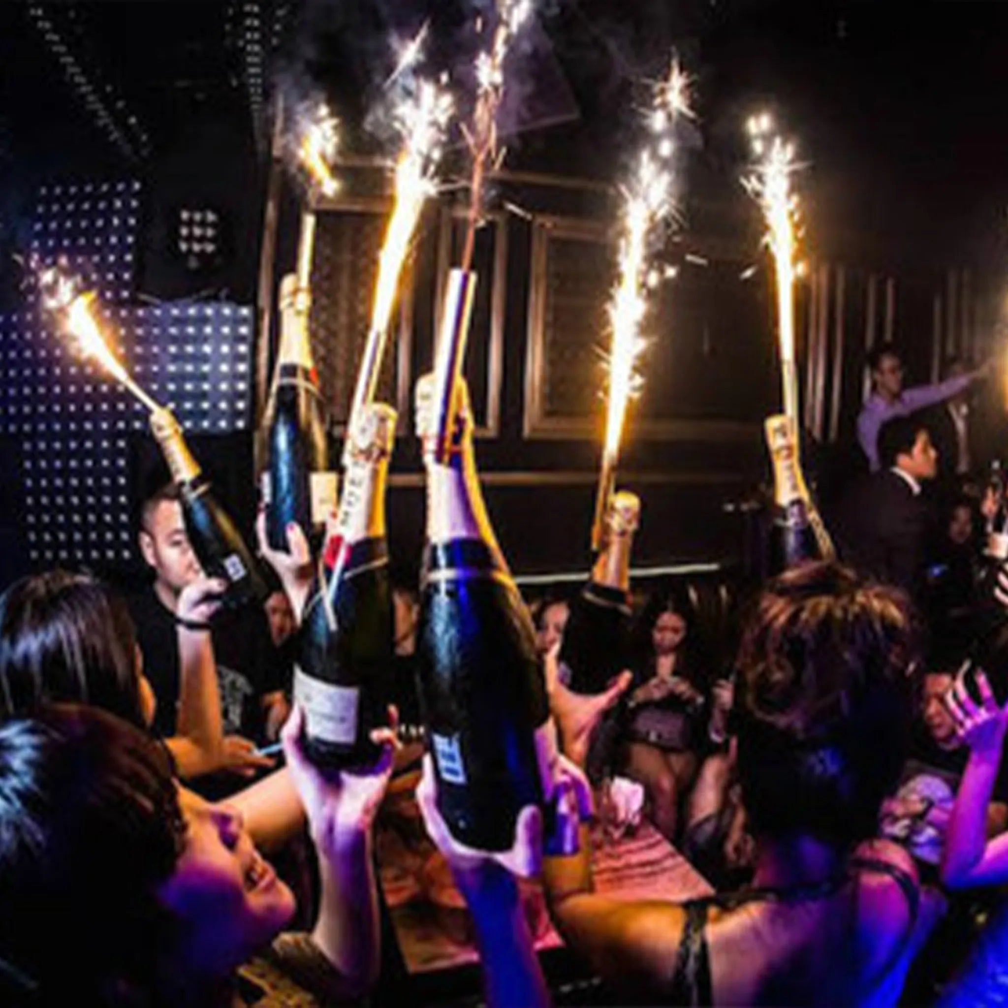 People celebrating with champagne bottles and sparklers in a dark indoor setting.